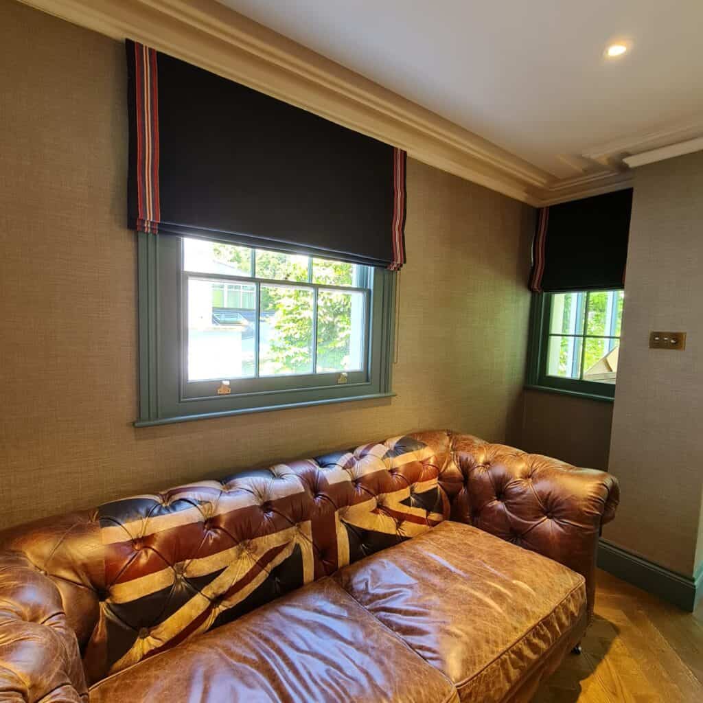 Black blinds half closed with red and white side stripe. Brown Leather sofa with union Jack