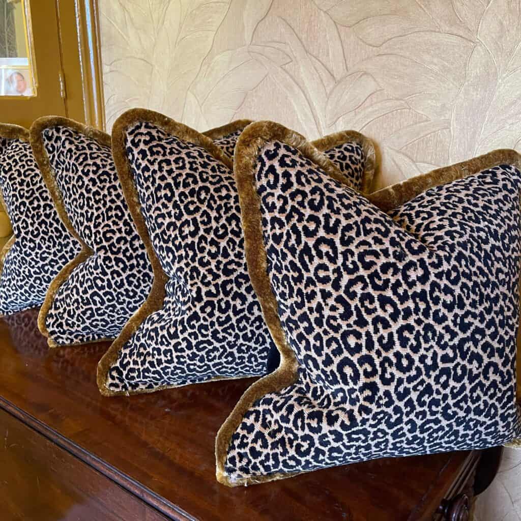 Four leopard cushions with trims on dark oak table